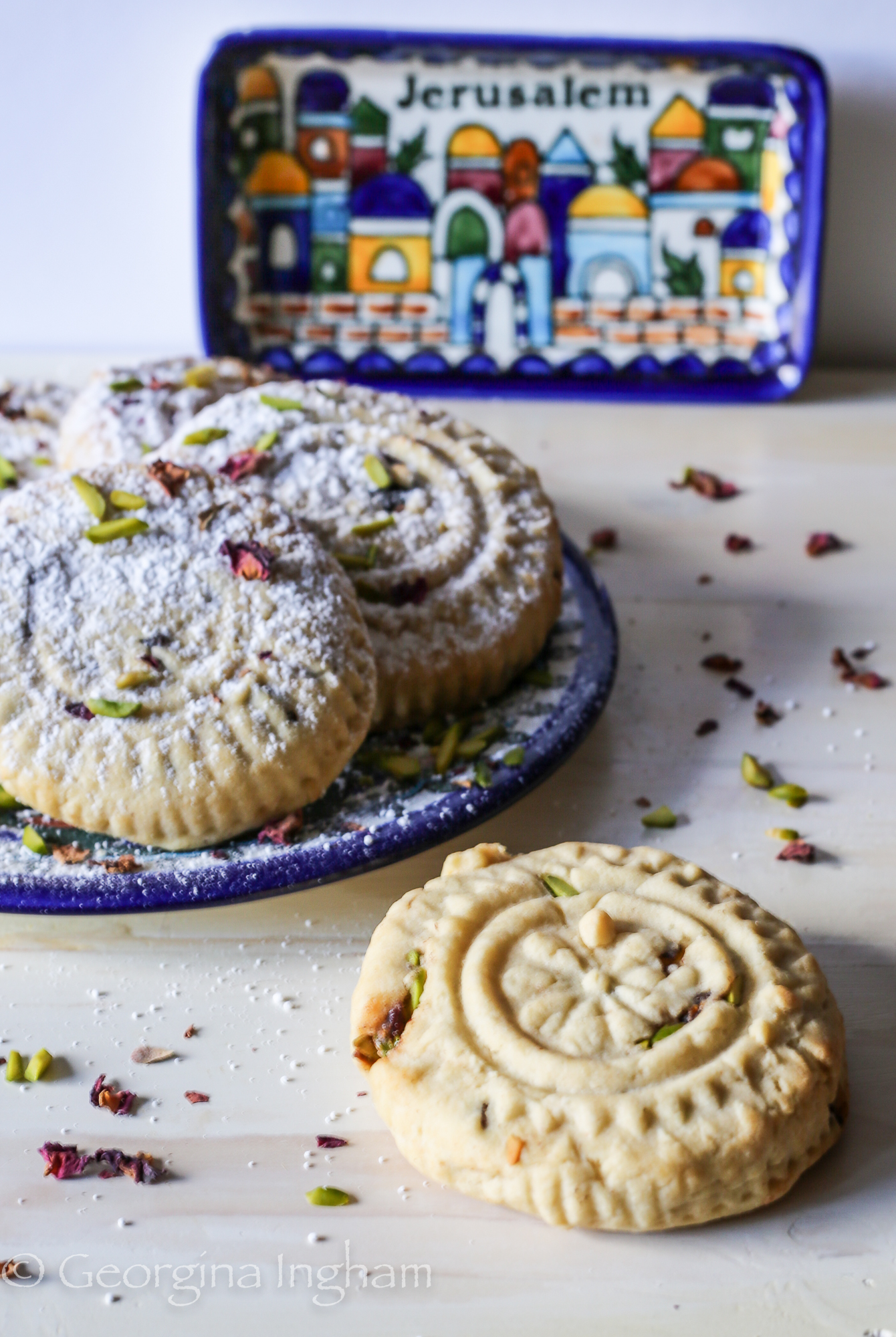 Plate of rustic homemade Ma'amoul cookies with a Jerusalem-themed plate subtly visible in the background, highlighting the textured pastries
